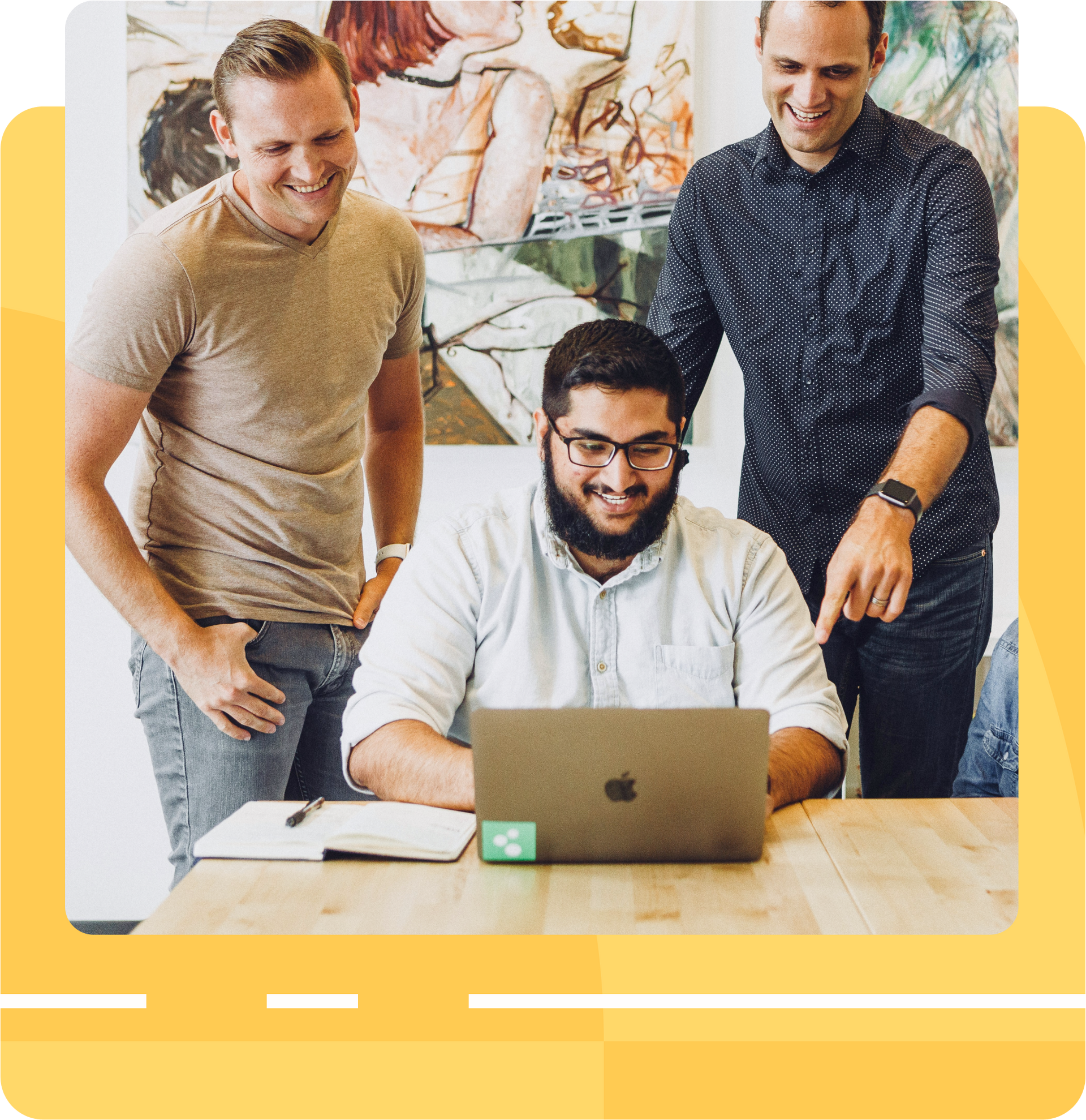 Three men are standing around a table looking at a laptop.