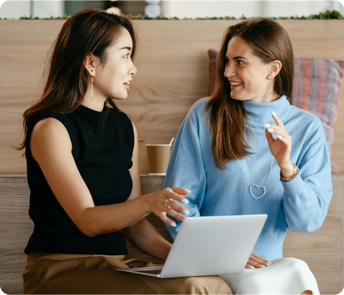 Two women are sitting next to each other with a laptop.