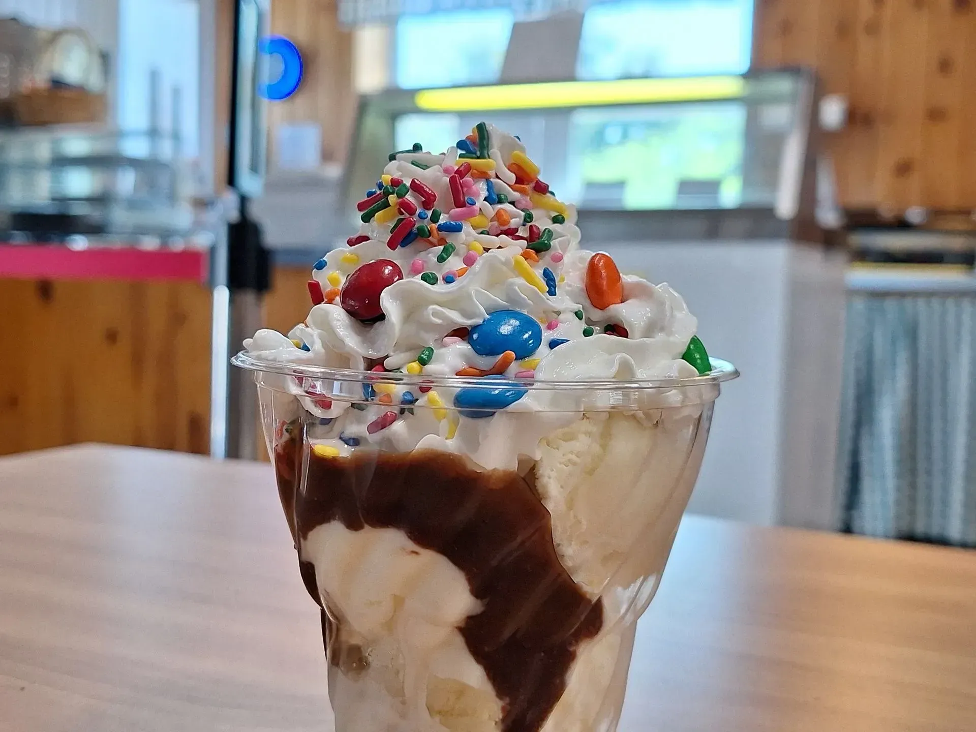 A close up of a sundae with whipped cream and sprinkles on a table.