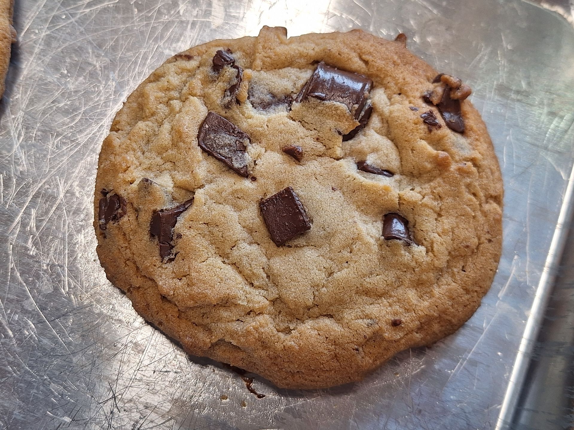 A chocolate chip cookie is sitting on a metal tray
