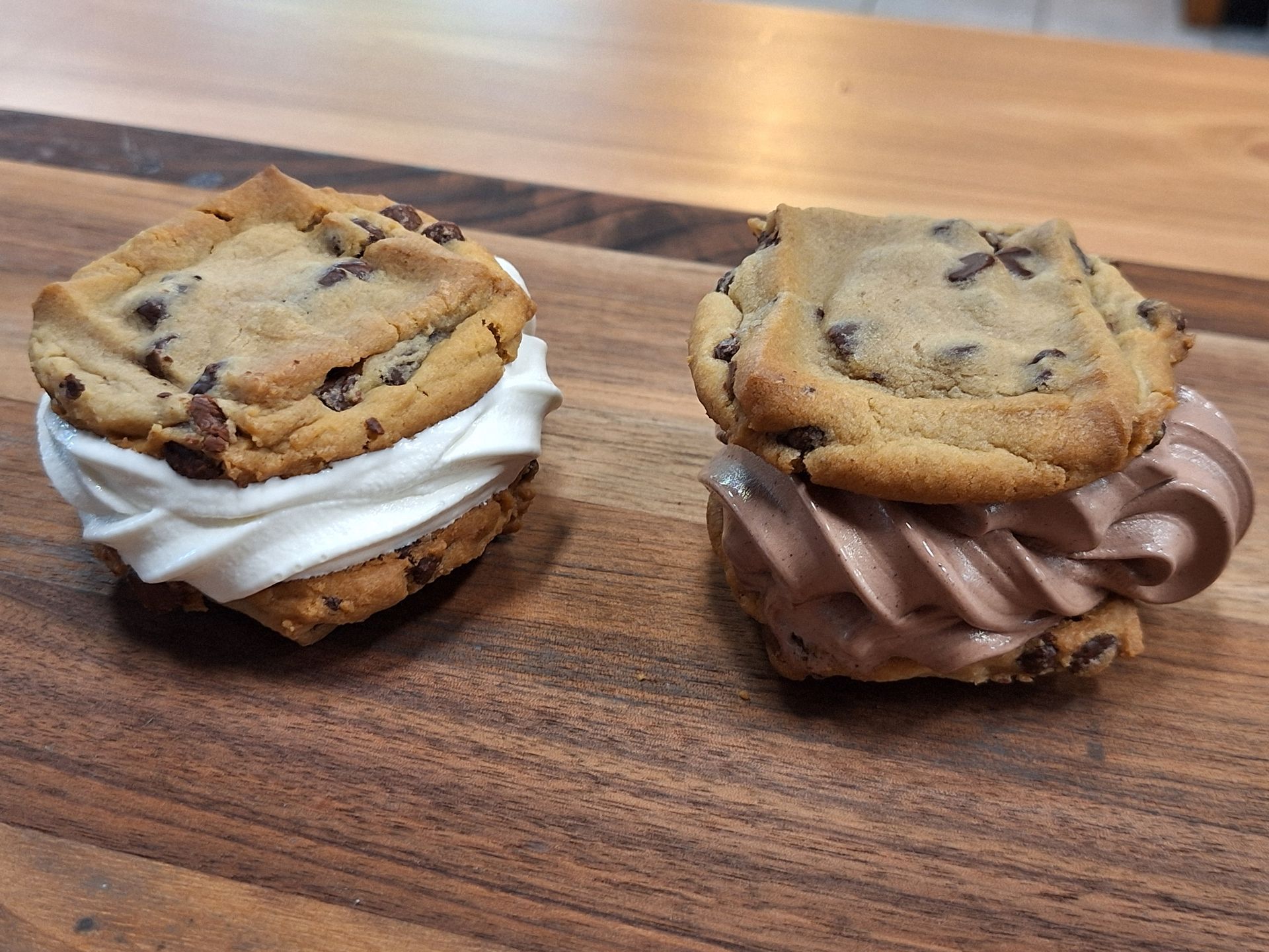 Two ice cream sandwiches are sitting on a wooden table.