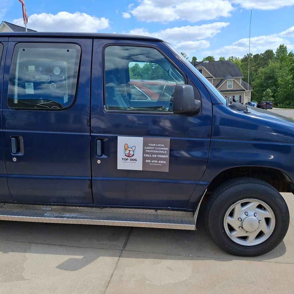Blue van with a logo on the side, parked on concrete. Sunny day with buildings in the background.
