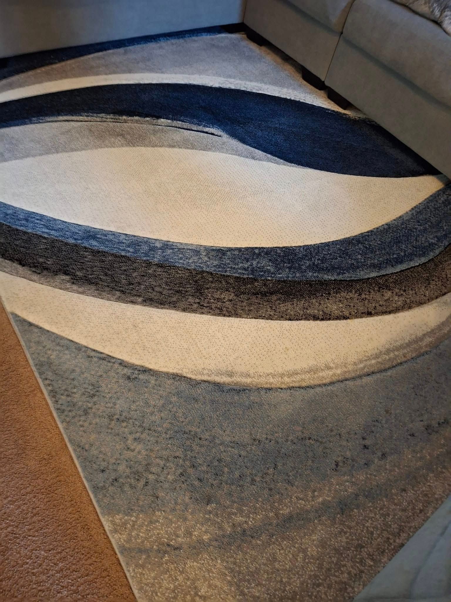 Blue, white, and gray patterned rug on brown carpet next to a gray sofa.