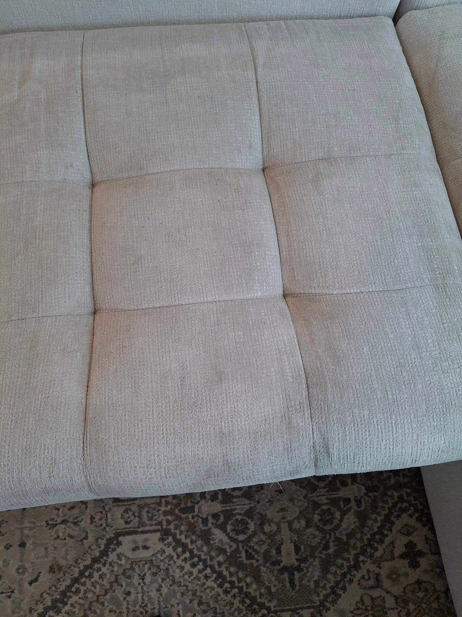 Close-up of a light gray, tufted fabric sofa with a patterned rug visible beneath it.