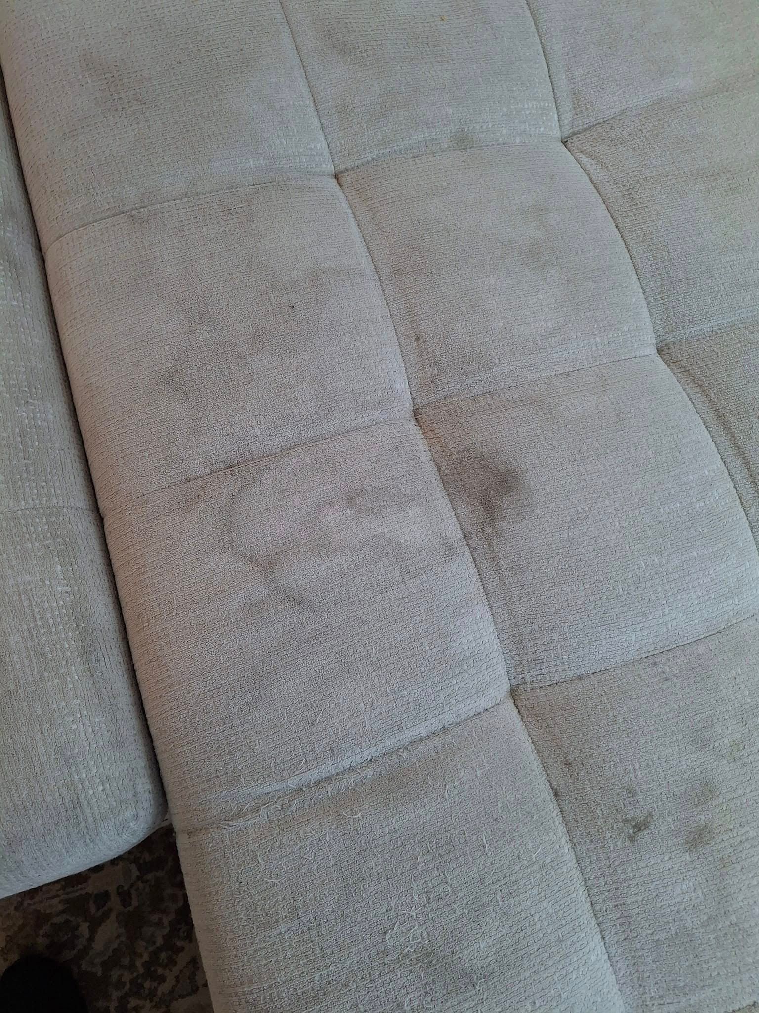 Gray, tufted sofa with visible wear and discoloration.