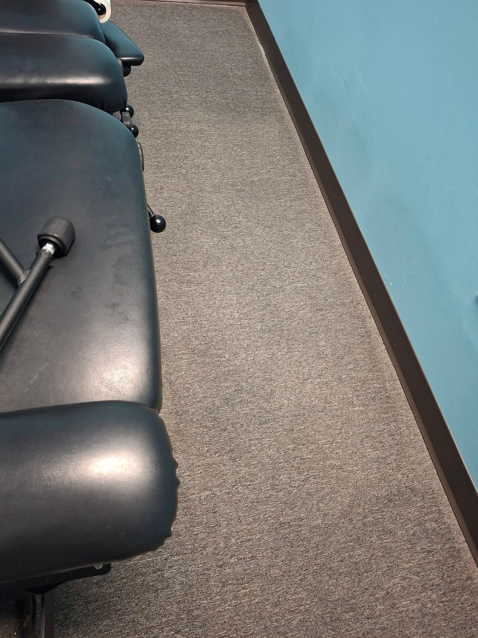 Black treatment table, gray carpet, and blue wall in a healthcare setting.