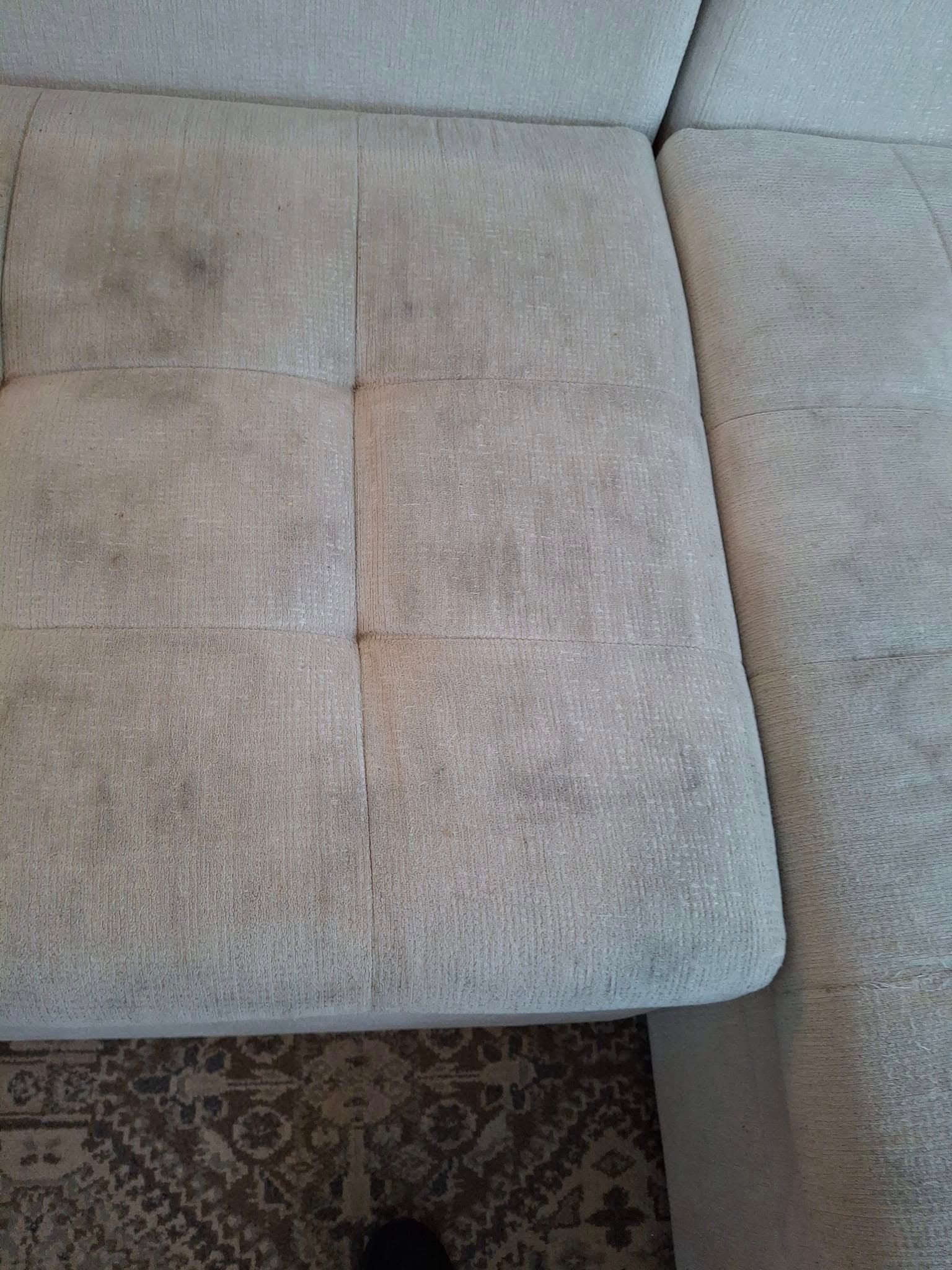 Dirty, light-colored sectional sofa with visible stains. A patterned rug is visible beneath the sofa.