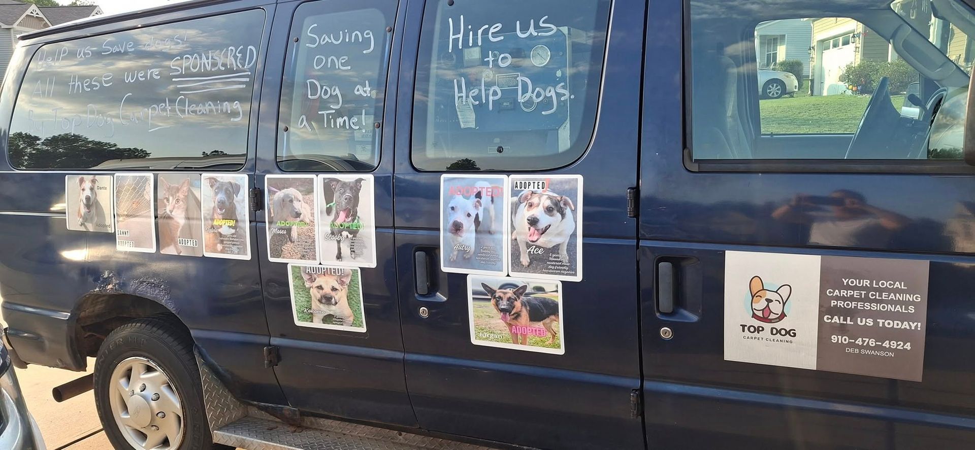 Blue van advertising dog-related services. Photos of dogs are affixed to the side with handwritten slogans.