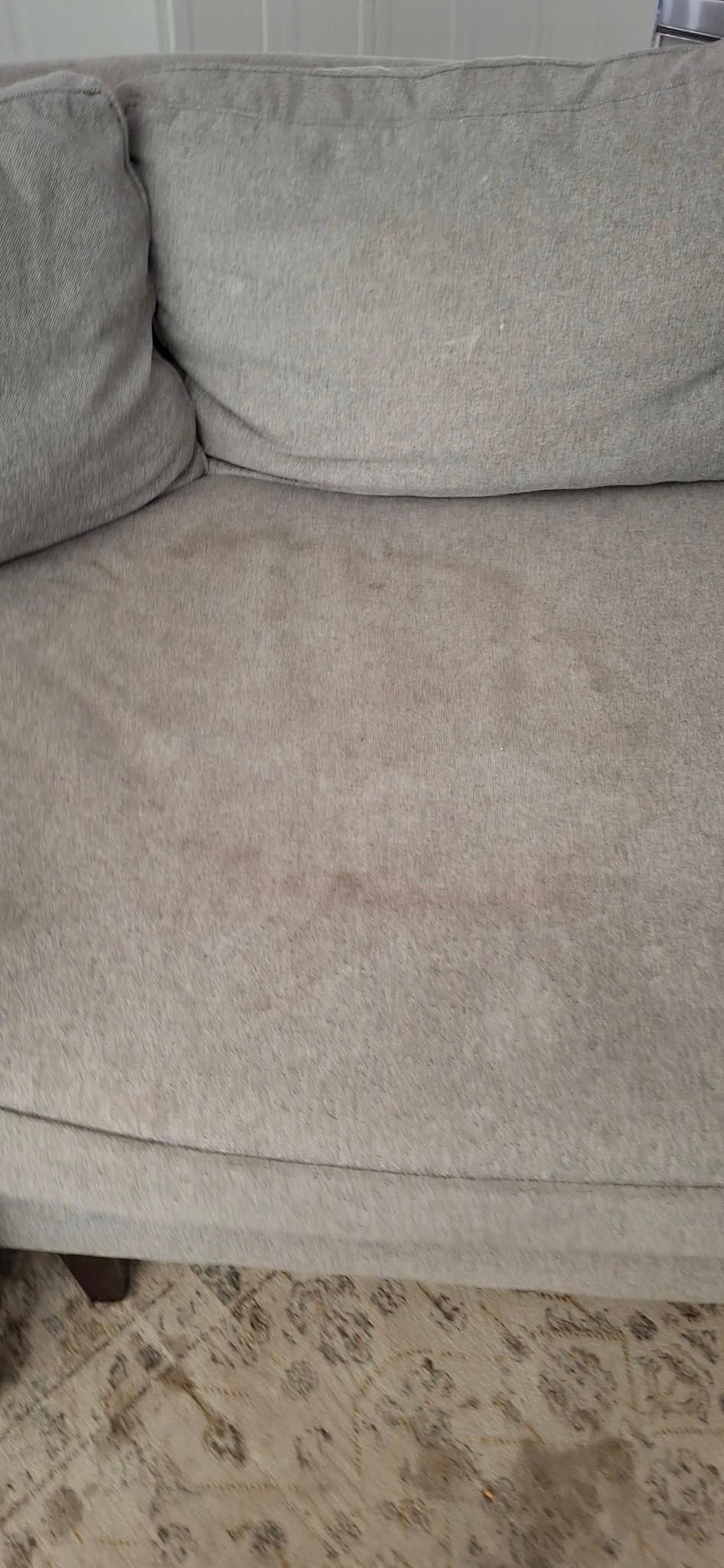 Close-up of a light gray sectional couch showing wear and tear, including stains.