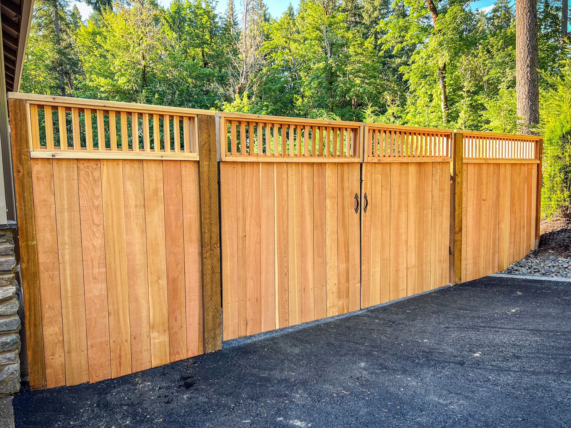 Wooden fence with gate, light brown, set against green trees.