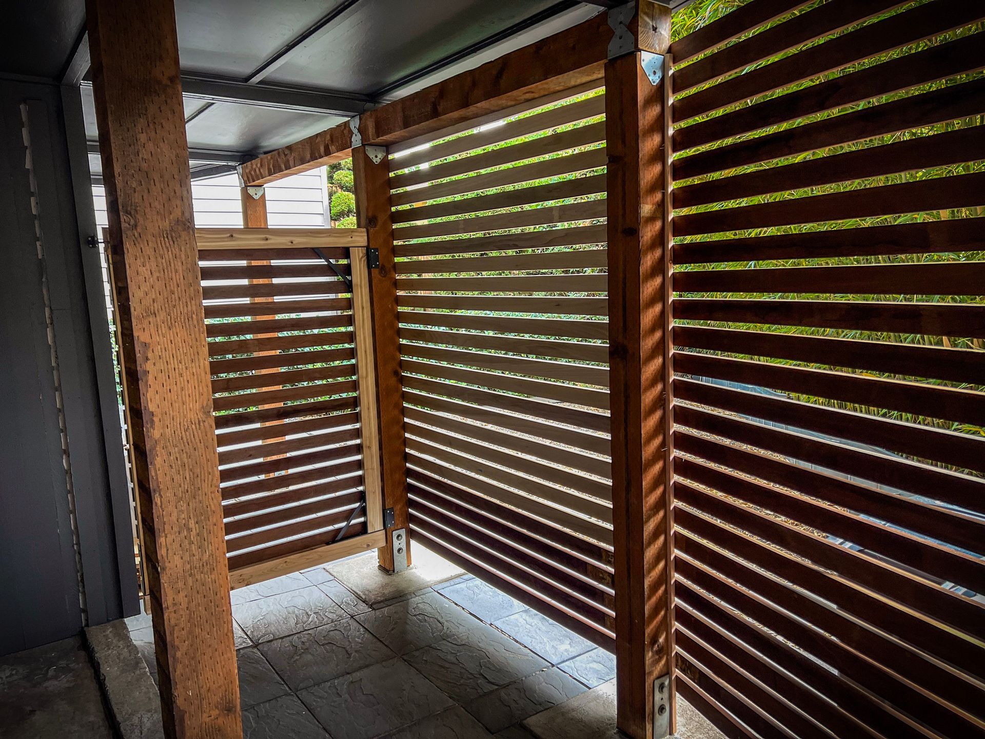 Wooden slatted privacy screens enclose an outdoor shower on a tiled floor.