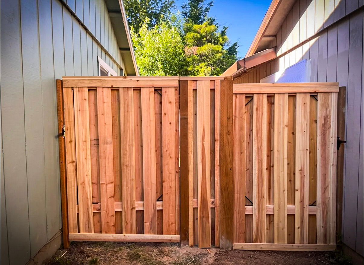 Wooden double gate between two beige walls, opening into a yard with greenery visible.