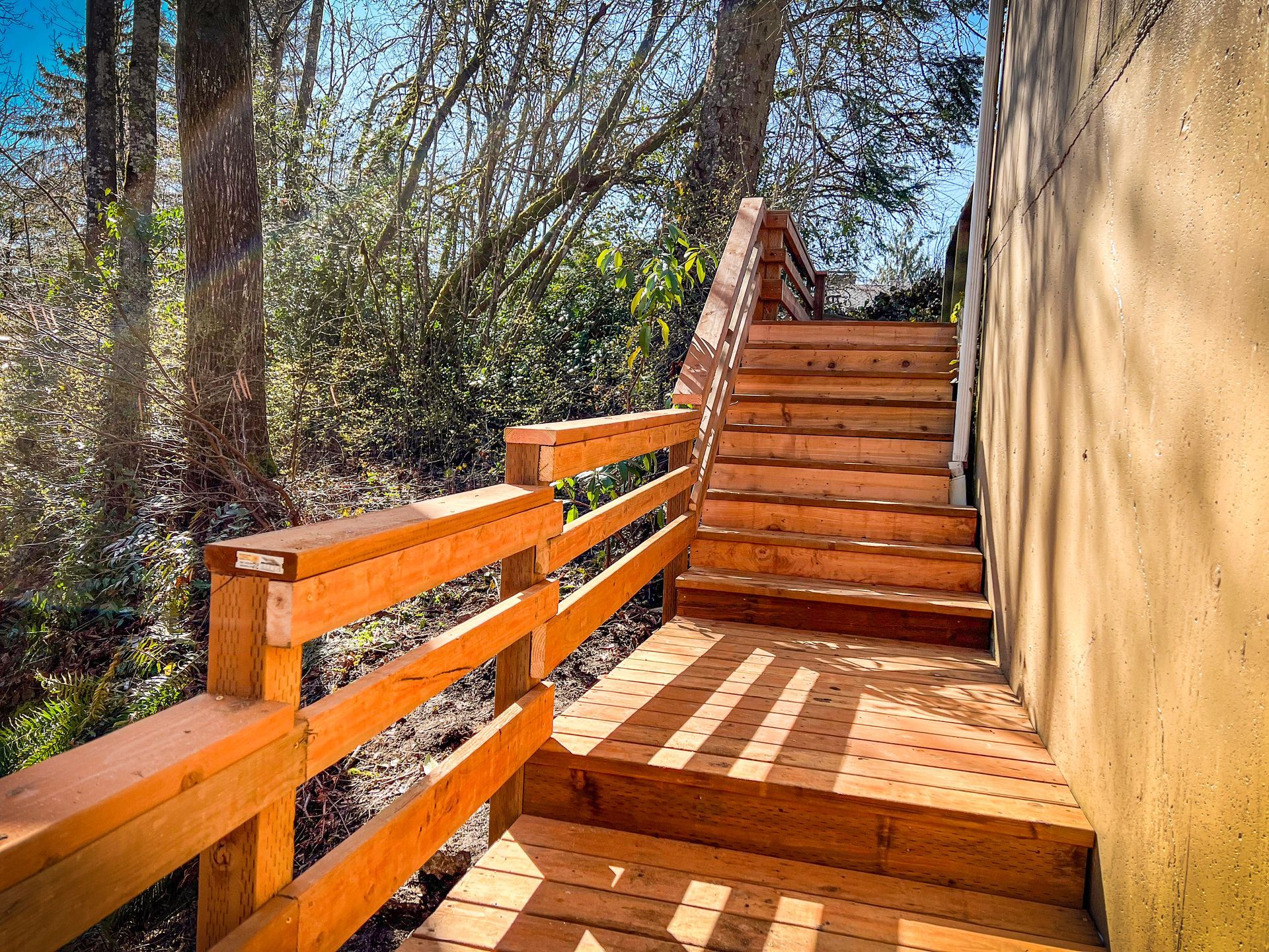 Wooden outdoor staircase with handrails leading upwards; sunlight casts shadows.