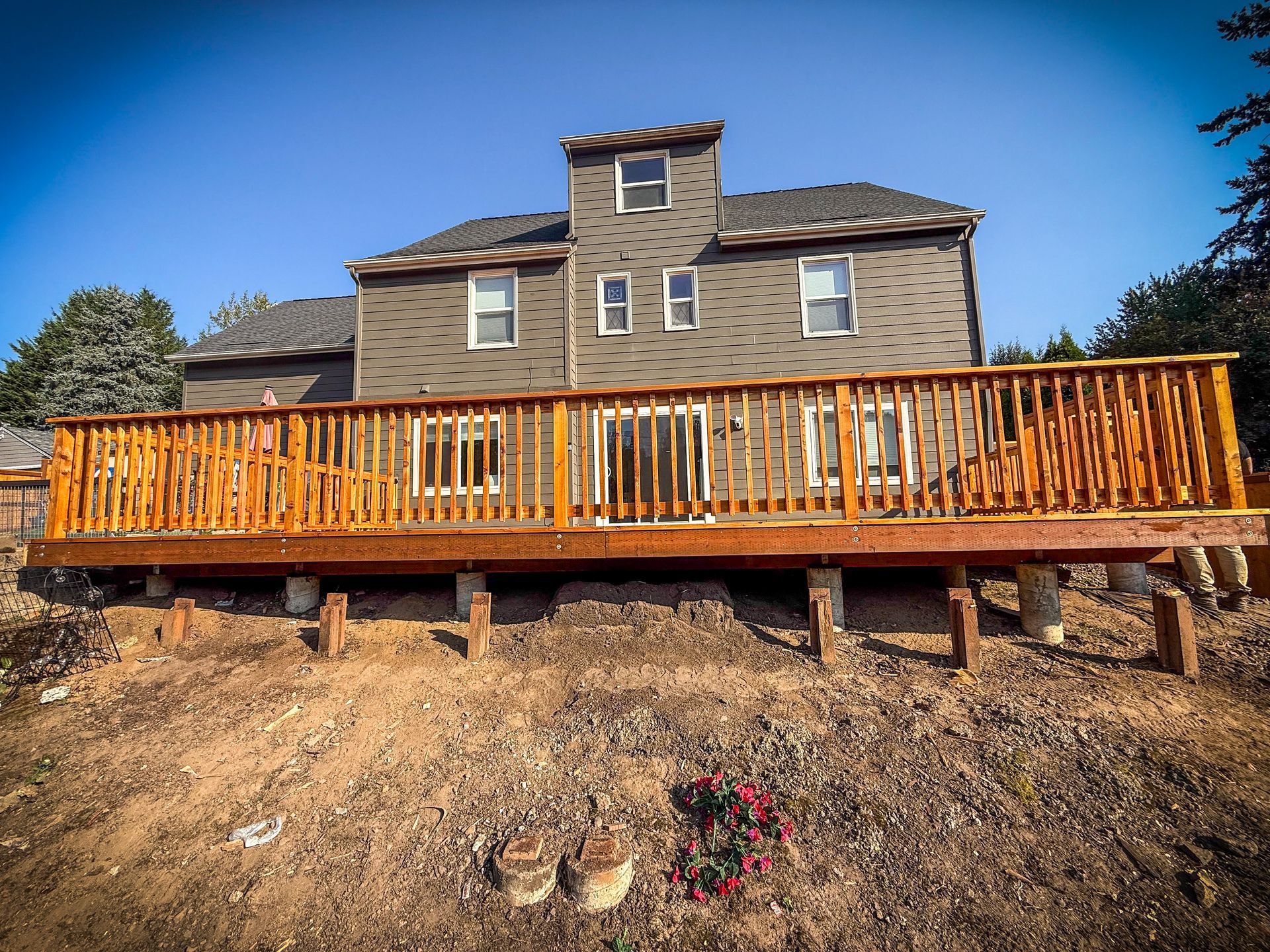 Back of a house with a large wooden deck. Deck is brown, house is gray with a blue sky.