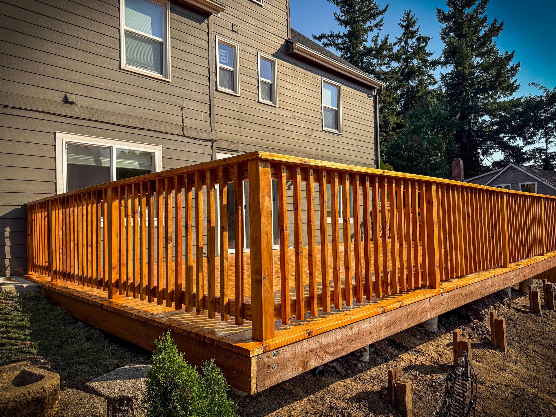 Wooden deck with railing attached to a two-story house, with green landscaping.