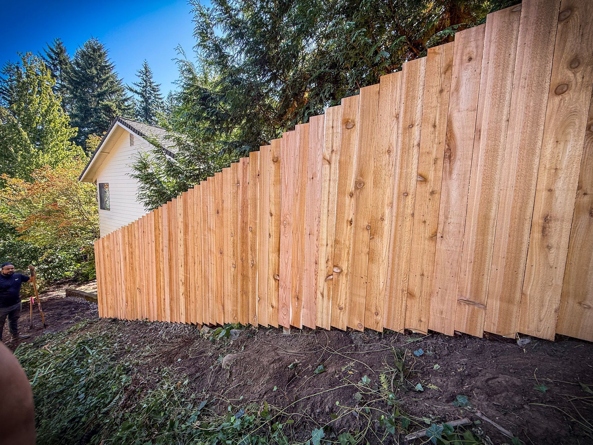 Wooden fence on a slope with a house in the background and a person on the left.
