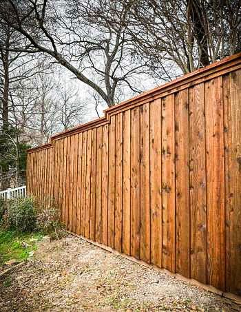 Wooden fence in a natural setting. Brown wood, some greenery, trees. Overcast sky.