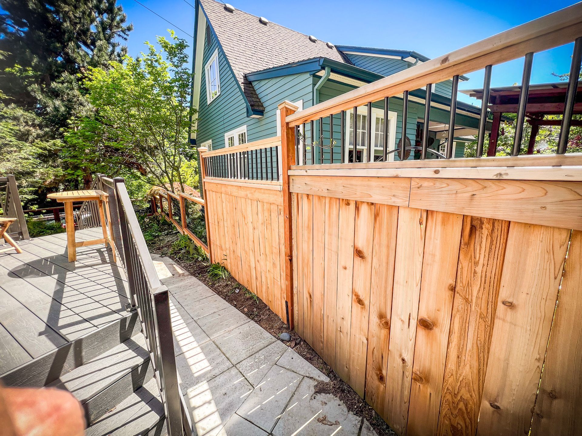 Wooden fence along a gray deck leading to a green house with a sloped roof.