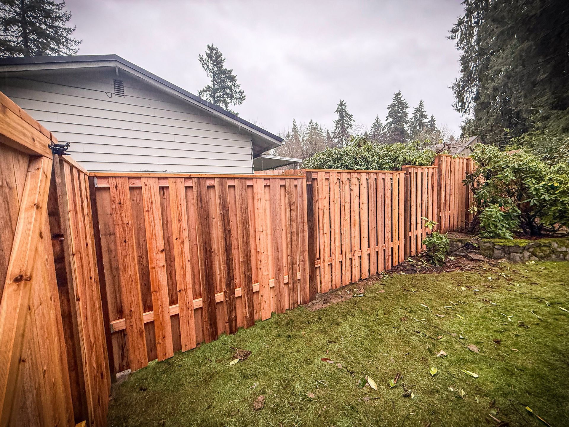 Wooden fence surrounding a grassy yard with a house and trees in the background.