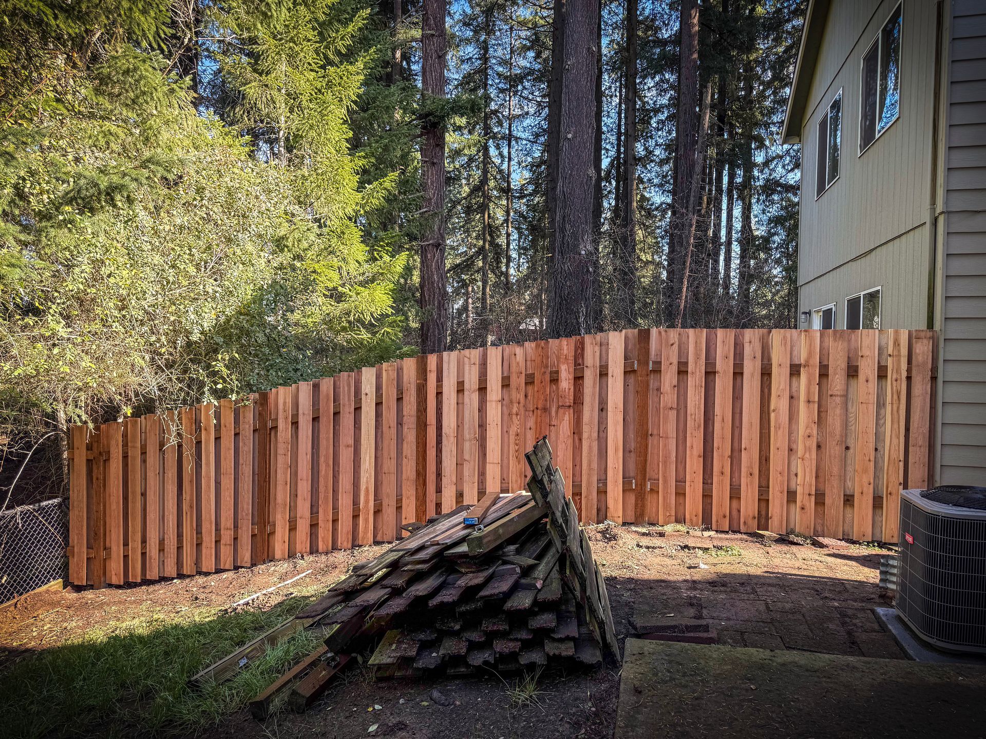 Wooden fence in a backyard setting, next to a house and trees.