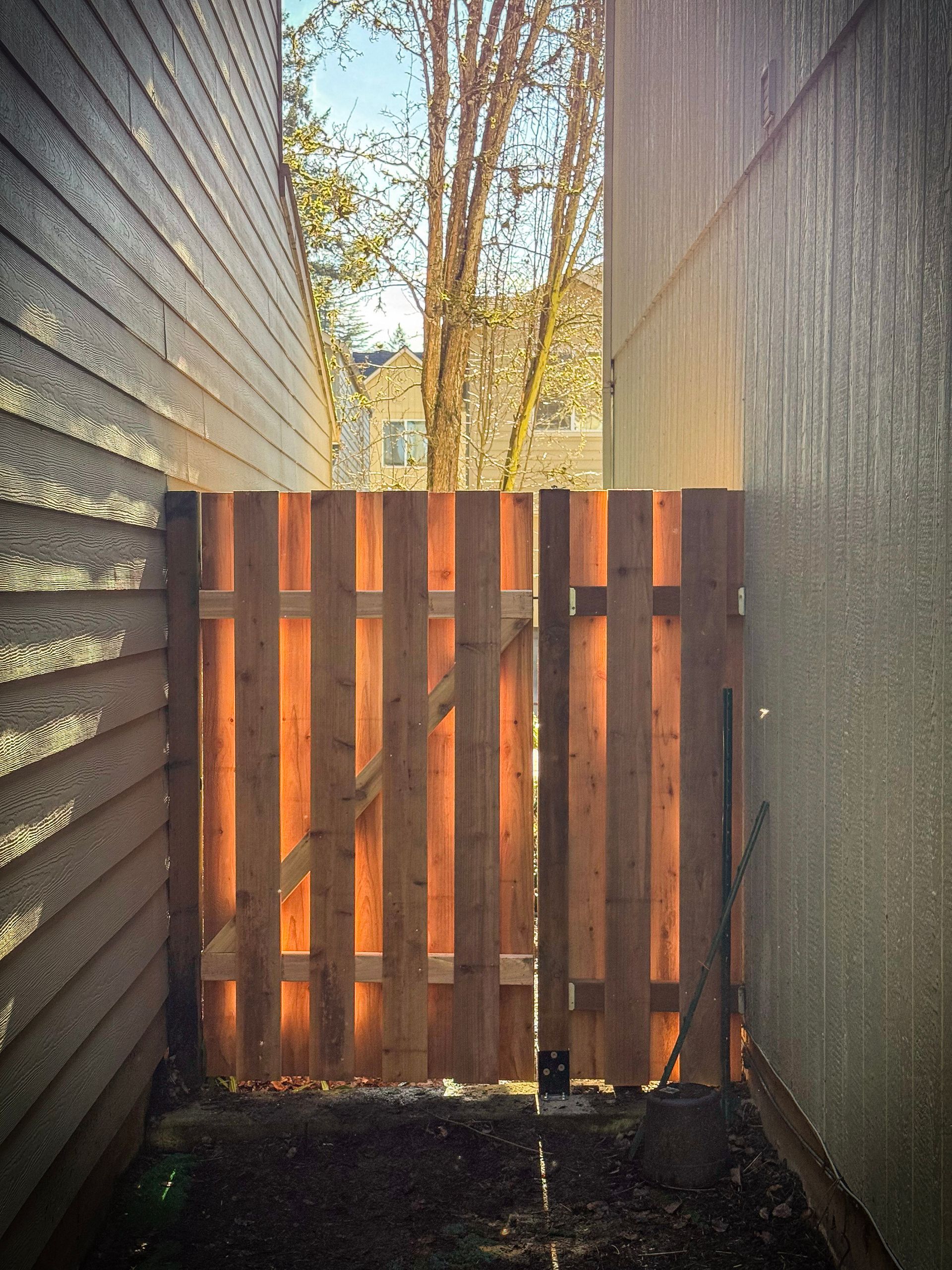 Wooden gate between two buildings, opening to a yard with trees.