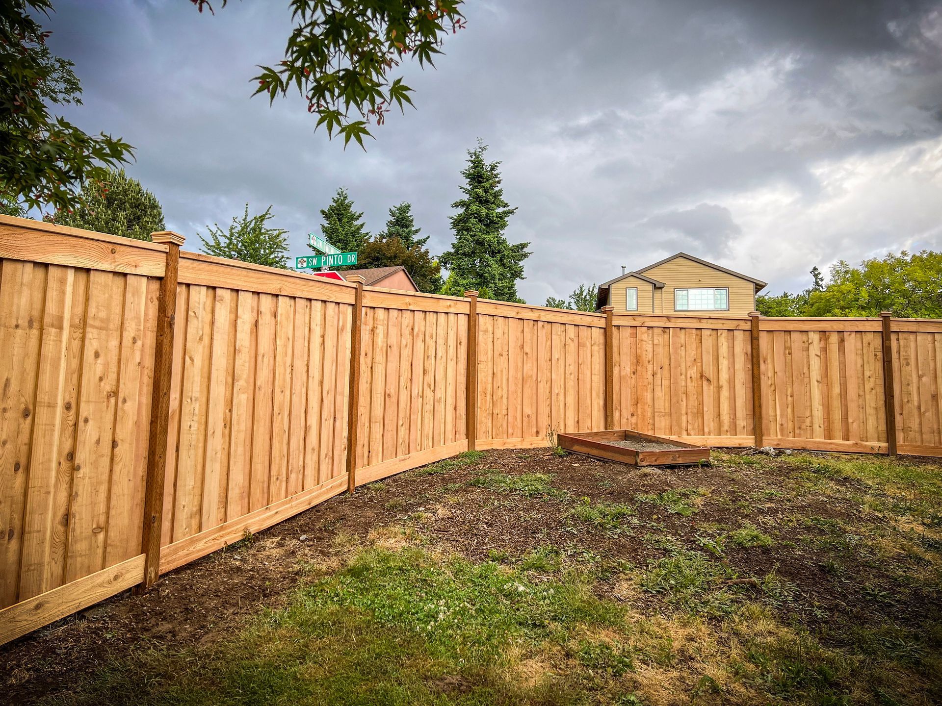 Newly built wooden fence in a backyard under a cloudy sky.
