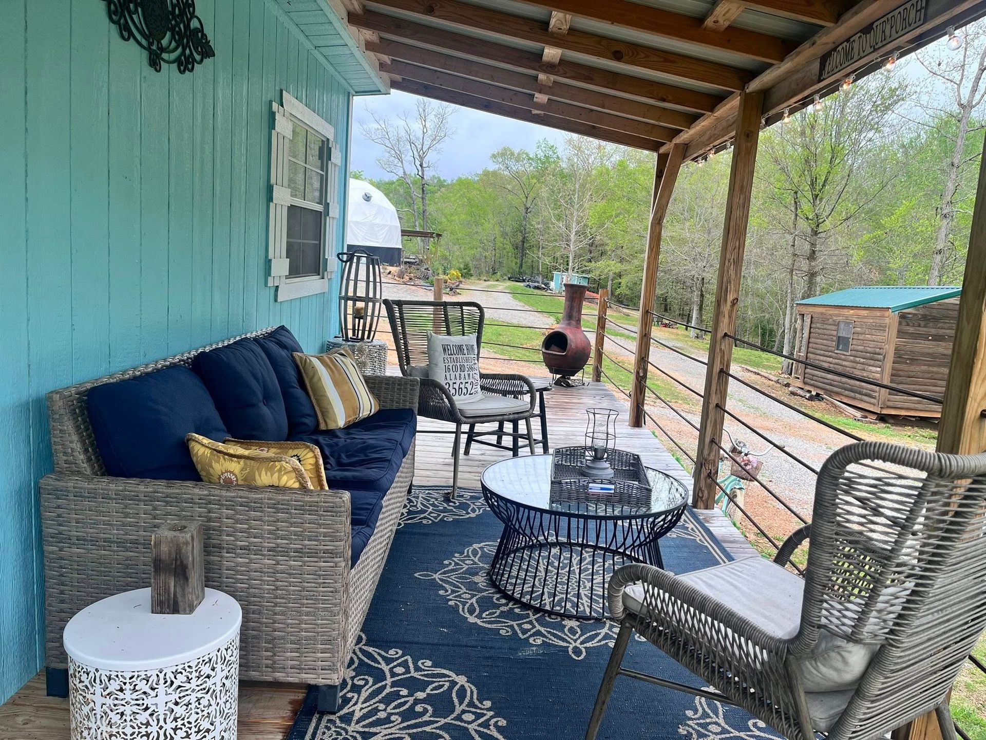 Porch with blue sofa, coffee table, and chairs. Turquoise siding, outdoor setting with trees.