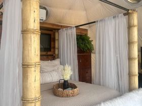 Cozy bed with bamboo posts and sheer curtains inside a yurt, a tray of flowers on the bed.
