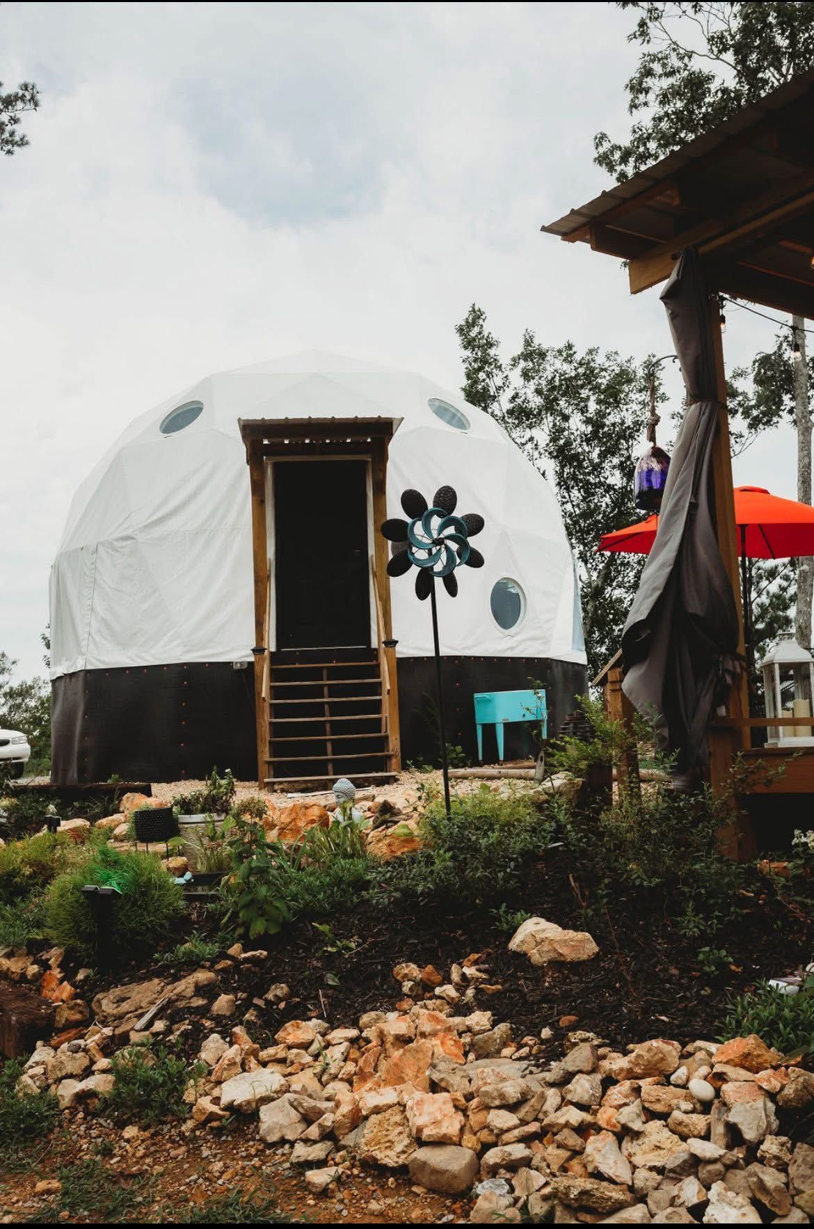 White geodesic dome with wooden door, set on a rocky hillside.