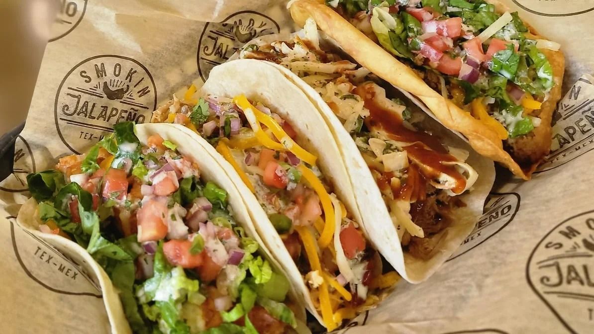 Four loaded tacos in soft shells on printed paper.