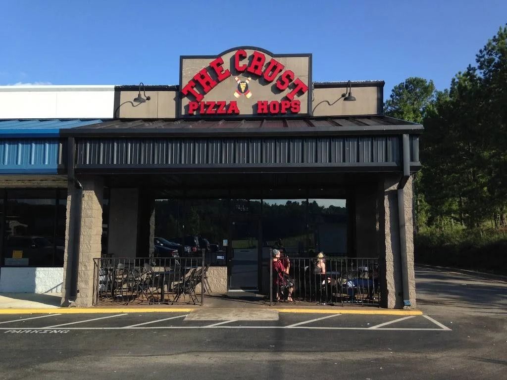 The Crust Pizza & Hops restaurant exterior with a black awning and sign. People are visible near the entrance.