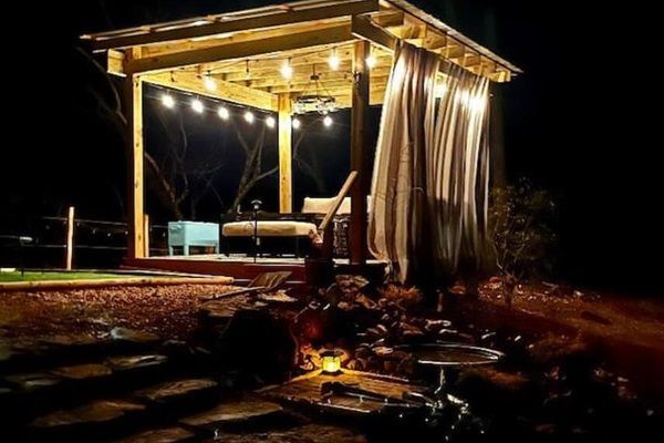 Wooden gazebo lit by string lights at night, with draped curtains.