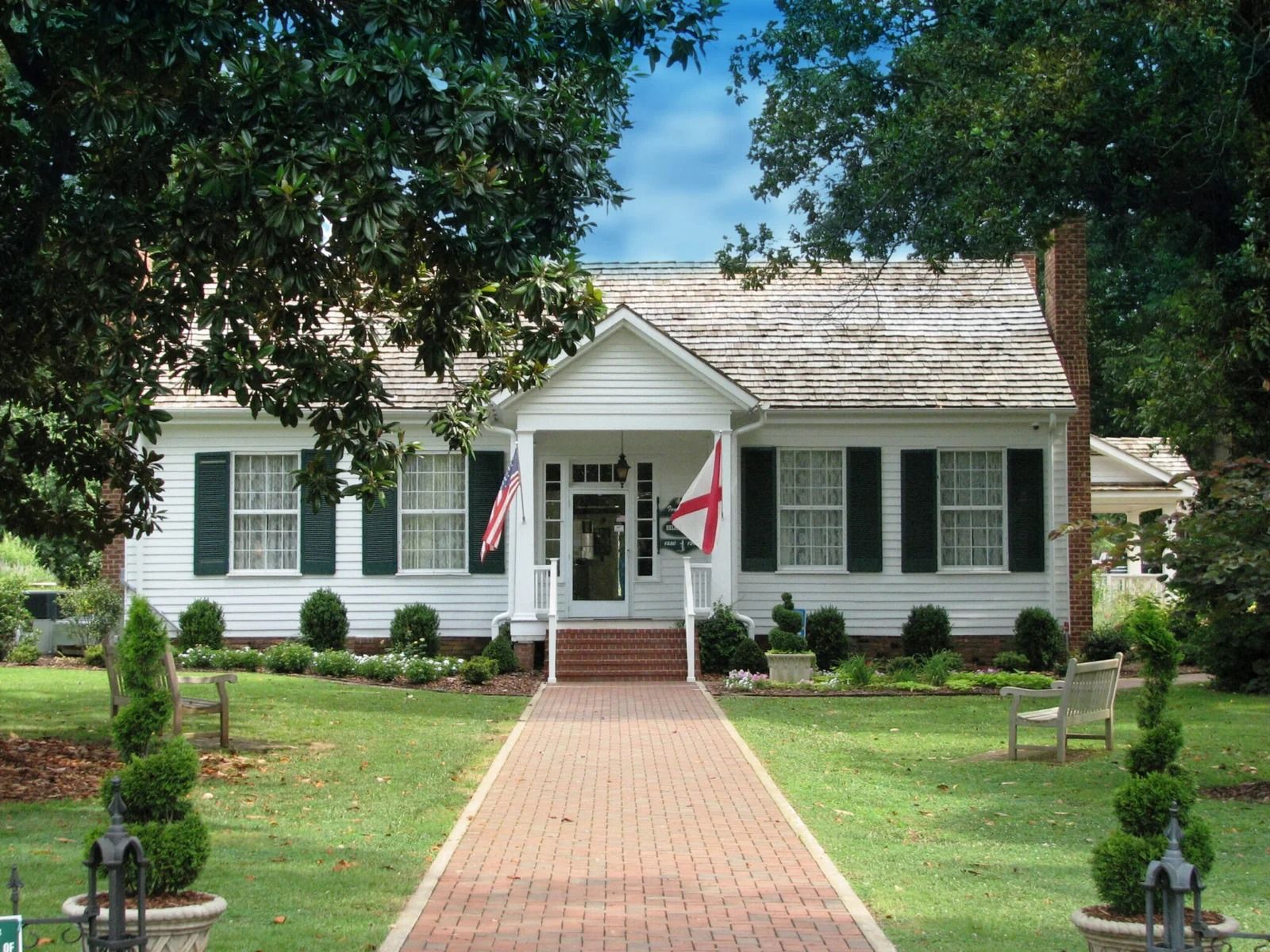 White house with green shutters, a brick walkway, and a well-manicured lawn.