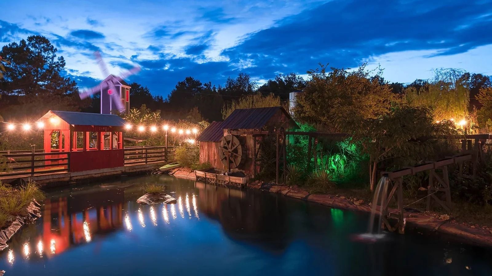 Nighttime scene of buildings, windmill, water, and lights reflecting in the water.