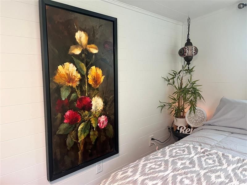 Large floral painting on a white wall, beside a bed and decorative lantern.