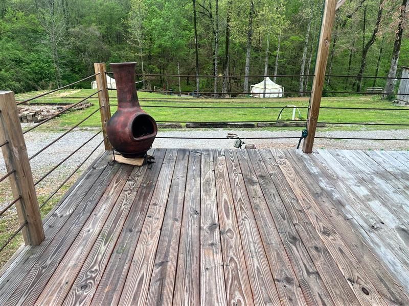 Wooden deck with weathered planks, an outdoor fireplace, and a forest backdrop.