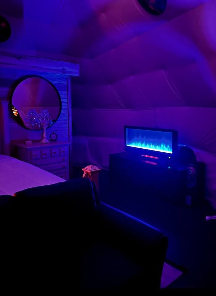 Room with a lit fireplace, mirror, and a bed bathed in blue light.