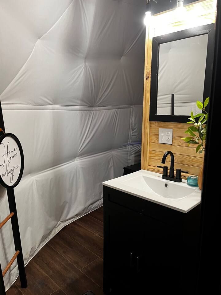 Small bathroom with a black vanity, wood accent wall, and a white, dome-shaped ceiling.