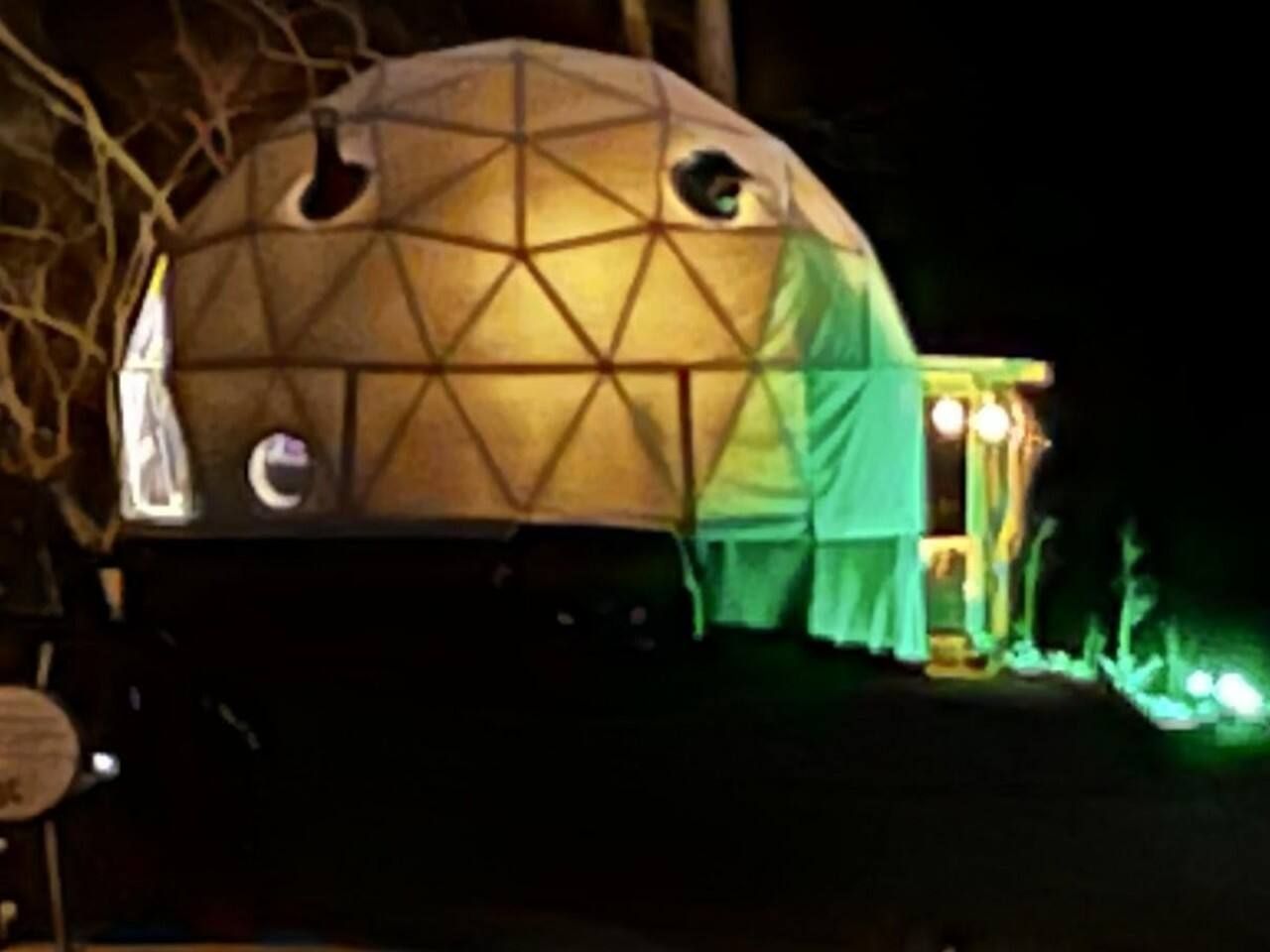 Geodesic dome structure illuminated at night with a small porch and green lights.