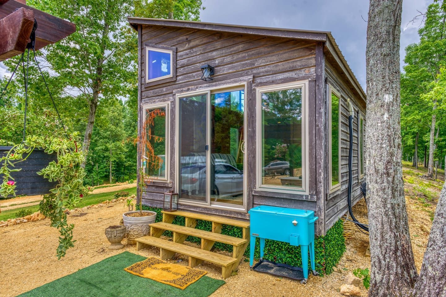 Small, weathered wooden cabin with large windows and a small front porch, surrounded by trees.