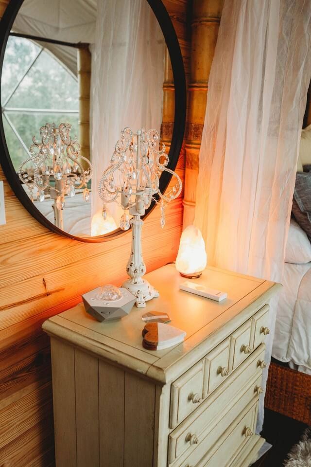 Cream-colored dresser with lamp, mirror, and salt lamp in a cabin bedroom.