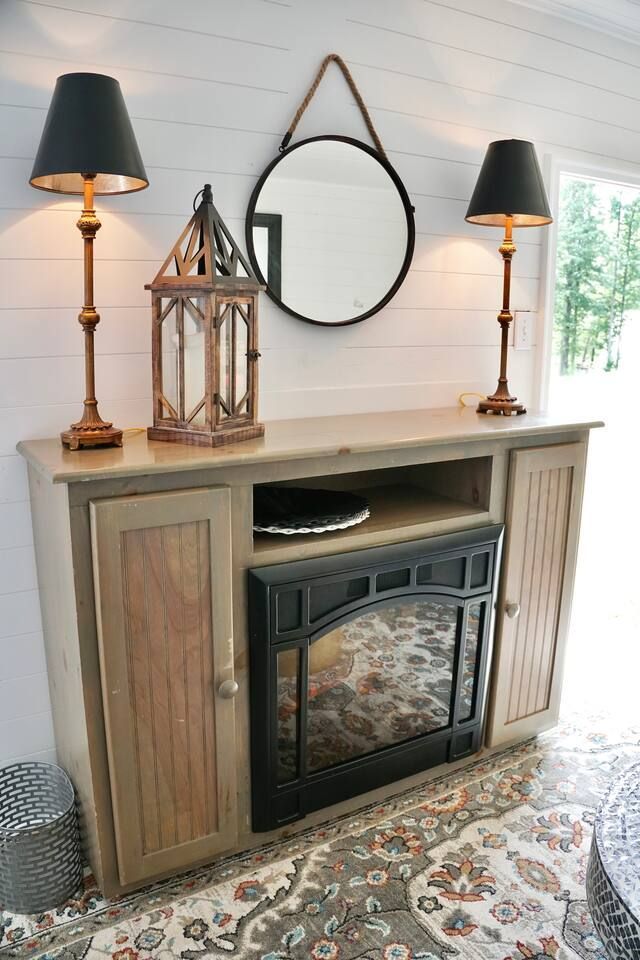 Fireplace with lamps, mirror, and decorative lantern on a wooden cabinet, in a room with white walls.
