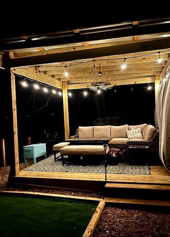 Outdoor patio at night, string lights, sofa, coffee table, rug, and turf grass.