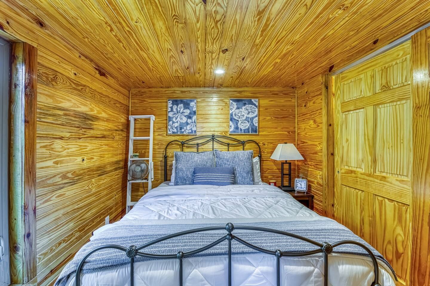 Bedroom with wood paneled walls, bed with black metal frame, and decorative wall art.