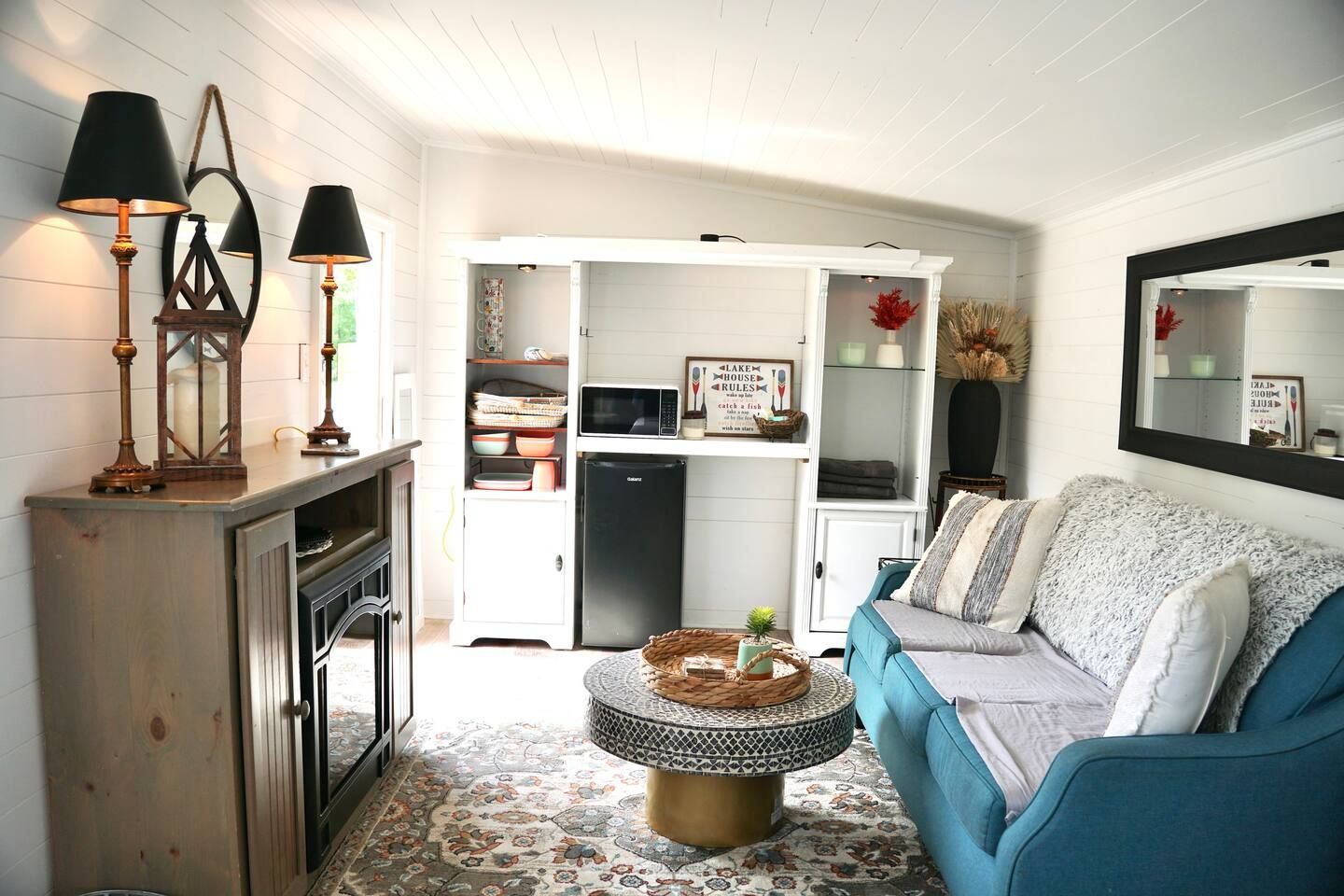 Small, cozy living room with turquoise sofa, fireplace, mini-kitchen, and decorative mirrors.