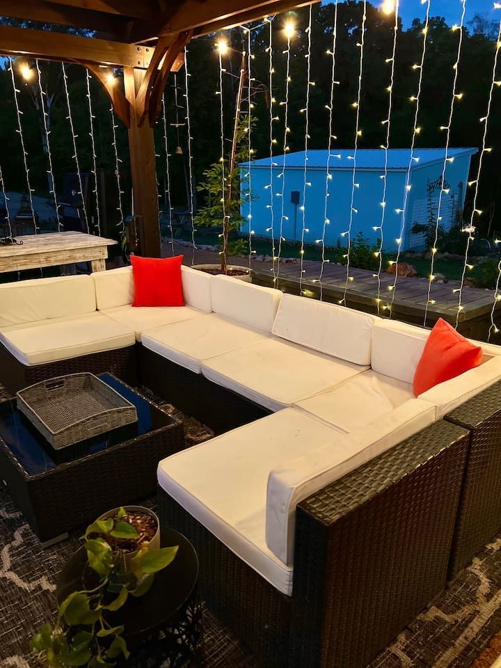 Outdoor sectional sofa with white cushions, red pillows, and string lights.