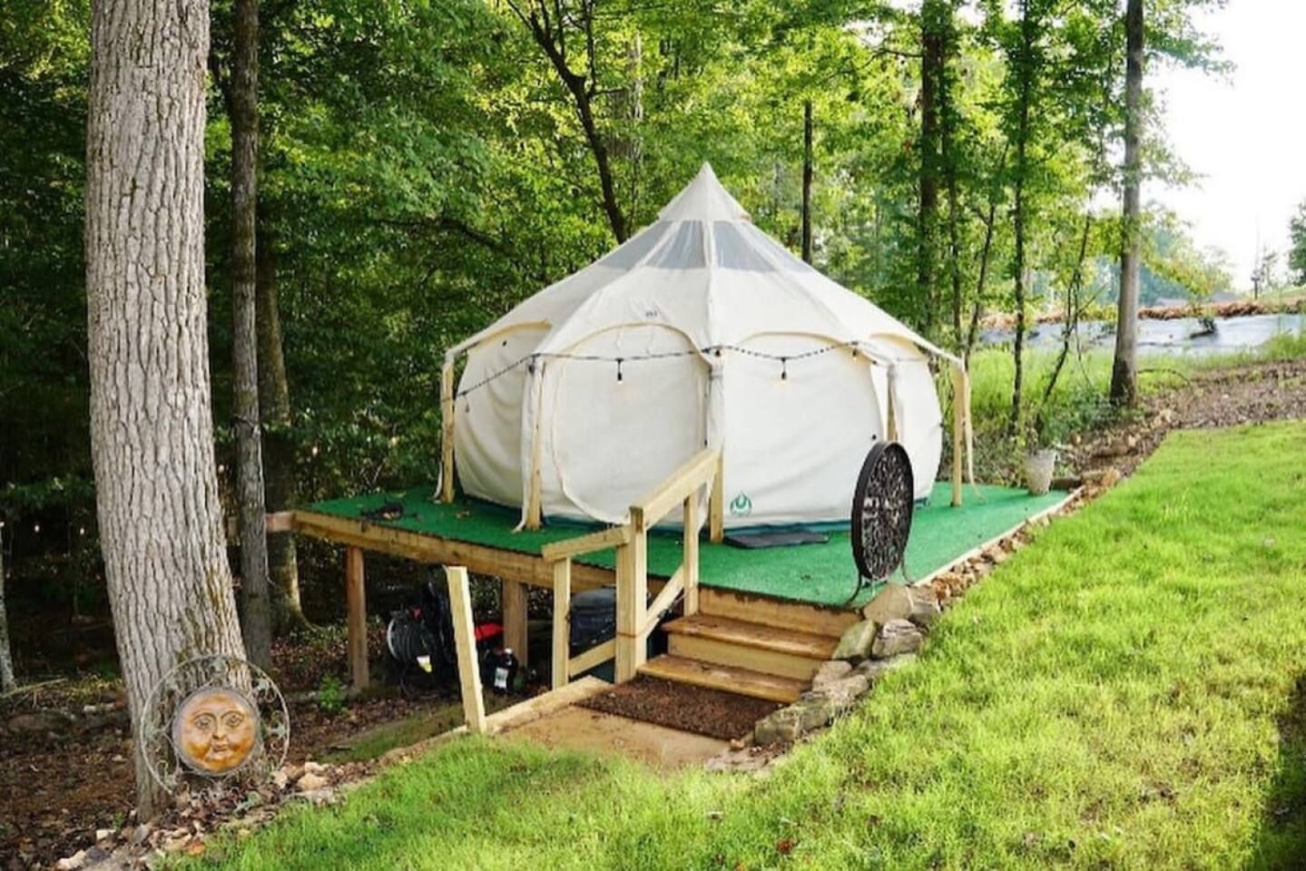 Canvas tent on a wooden deck in a wooded area with stairs leading up to it.