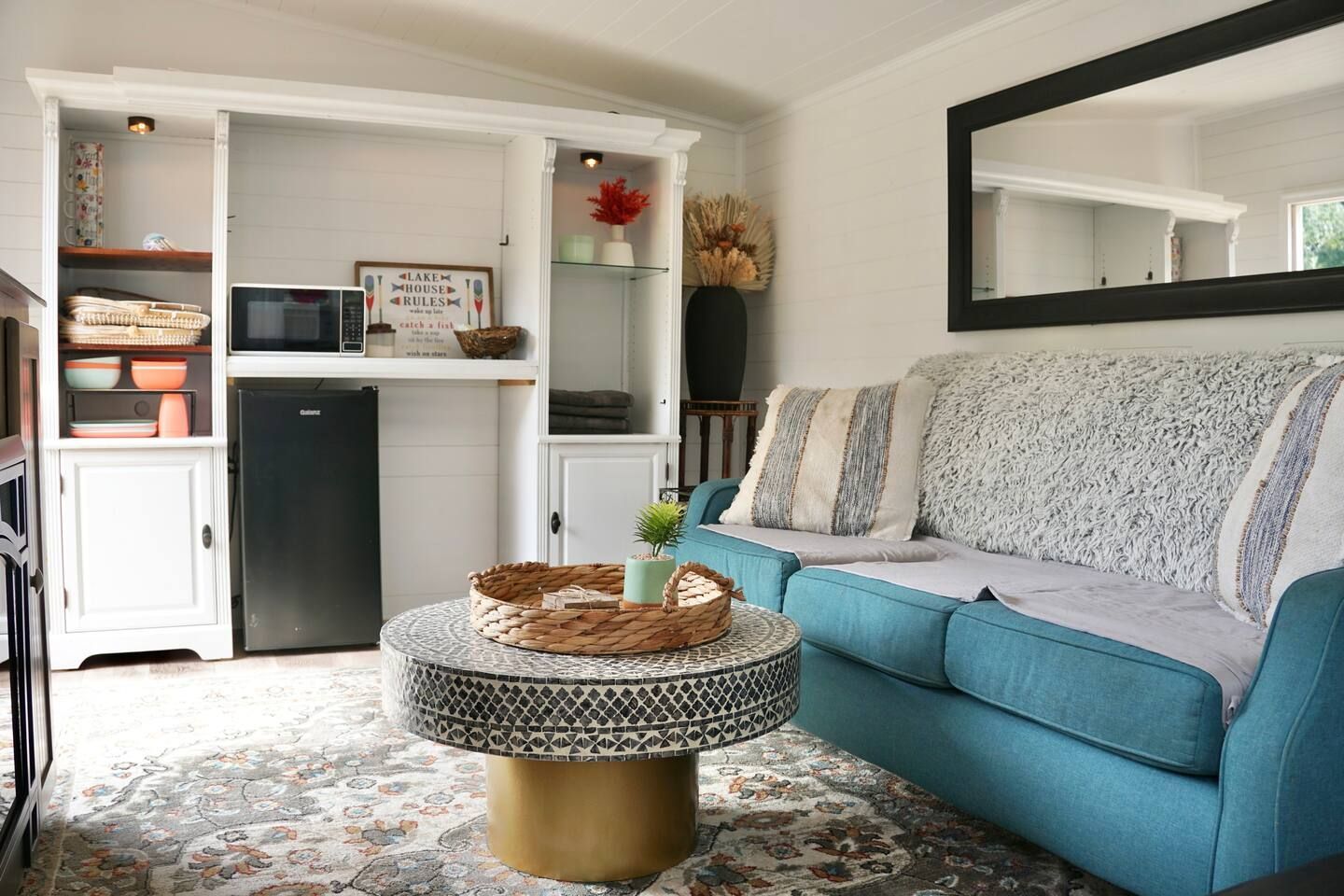 Cozy living room with blue sofa, white cabinet, patterned rug, and round coffee table.