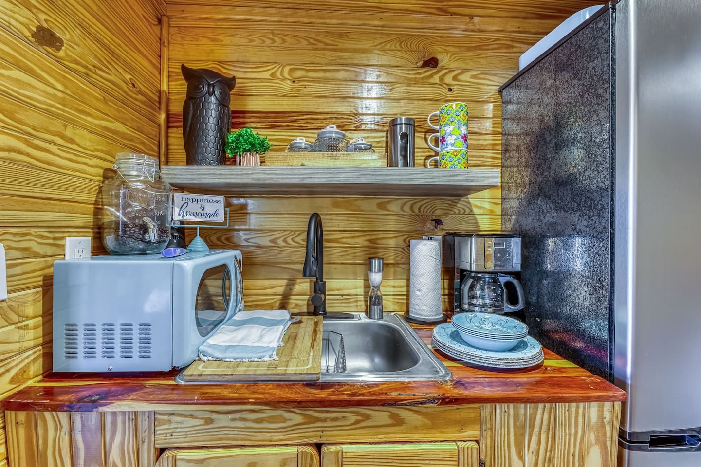 Small cabin kitchen with sink, microwave, coffee maker, and shelf with decorations.