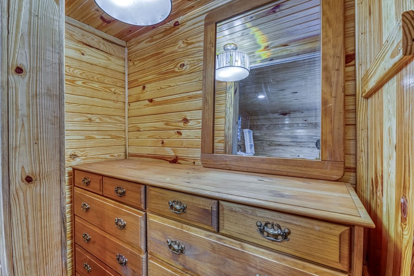 Wooden dresser with mirror in a room with wood-paneled walls and a light fixture.